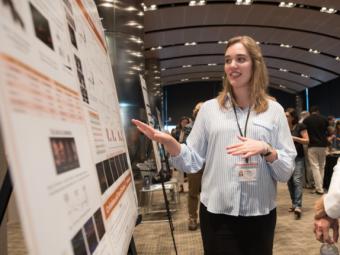 Ellie Mackintosh, a white woman with collared shirt and black pants explaining to someone not pictured the research on her poster