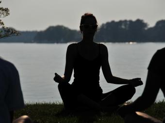 silhouette of person doing yoga in front of lake
