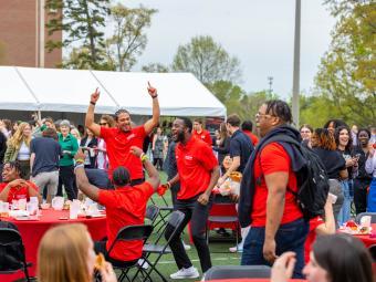People jumping and smiling around a table in red Davidson shirts
