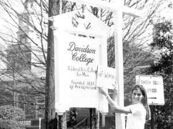 Woman holds a sign over another sign