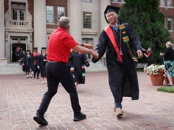 Student high-fiving an adult while wearing graduation regalia