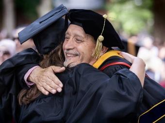 Professor and student hug while wearing commencement regalia