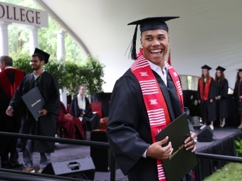 Student smiles at camera while holding diploma