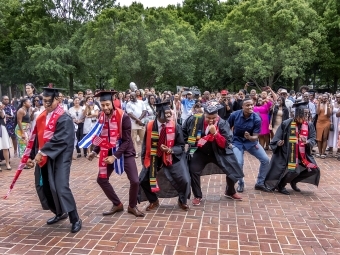 Men in caps and gowns pose after graduation ceremony