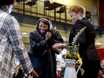 Three women smile and embrace while wearing graduation regalia