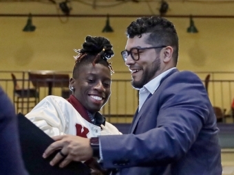 Two men hug and smile while holding a diploma