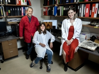 Two students and a professor stand around a lab together smiling