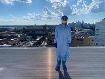 Lilly Sirover ’24 wearing medical scrubs standing on a rooftop platform overlooking many buildings