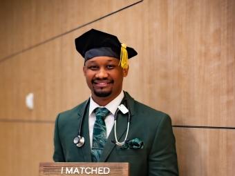 a young man wears a graduation cap and suit and holds a sign that says "I matched Pediatrics at Childrens Hospital of Philadelphia"