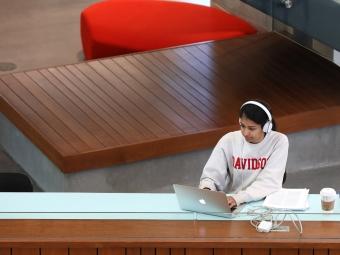 student wearing a Davidson sweatshirt and headphones works on a laptop in a modern academic building