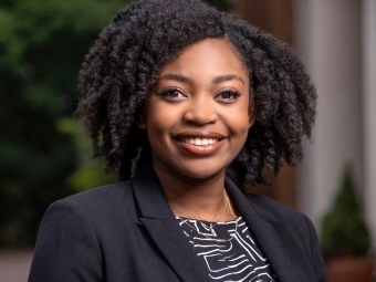 a young Black woman wears a black blouse and blazer while smiling