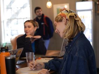 two students smile while working in a coffee shop