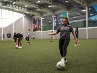 a student wearing a Davidson shirt kicks a soccer ball in an indoor field