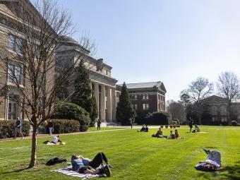 students sitting on a green lawn in front of a brick building on a sunny day