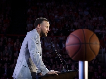 a man in a grey suit speaks into a microphone on a stage
