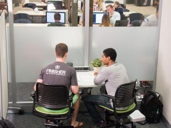 two students work in a glass cubicle while chatting