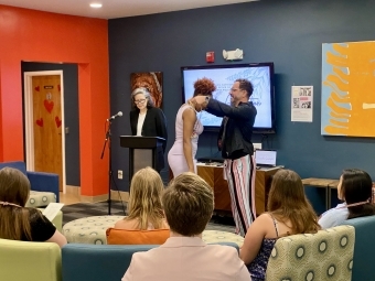 an adult presents a student with a graduation cord while another adult speaks into a lectern