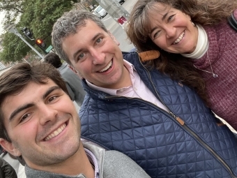 a group of three people stand together smiling on a city street