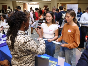 two young women talk to an older woman while holding papers at a job fair