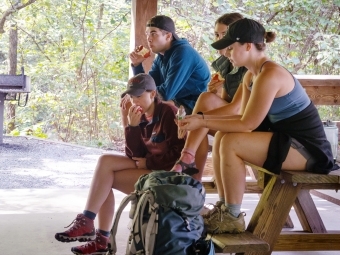 a group of young men and women sitting on picnic benches wearing hiking clothes