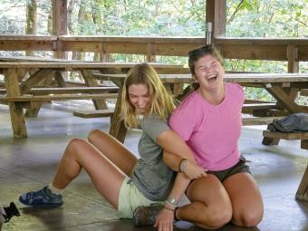 two young women participate in a team bonding activity in a camping lodge