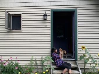 a young woman sits on a staircase outside of a house with a dog surrounded by flowers