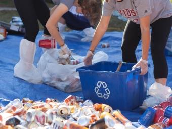 two young people holding recycling bins while sorting through piles of trash