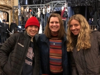 three young women stand together smiling in a theater