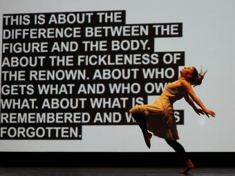 a dancer moves in front of a screen with a block of text on it