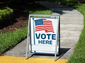 "Vote Here" sign in front of a sidewalk
