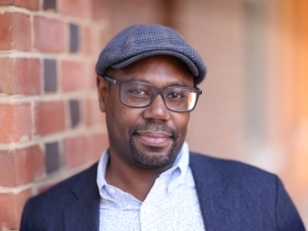 a middle aged Black man wearing glasses, hat and collared shirt with jacket