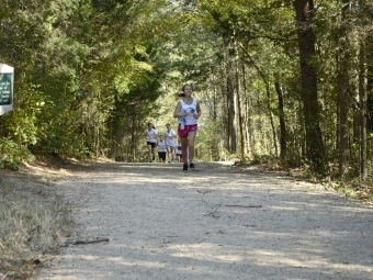 a young woman runs on a cross country trail in the woods