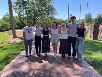 a group of young men and women standing together and smiling on a brick pathway
