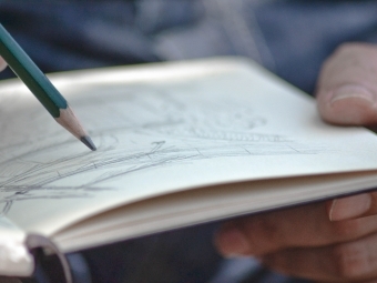 a hand holding a notepad while sketching with a pencil