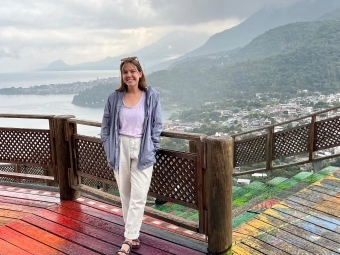 a young white woman standing on a wooden deck overlooking mountains and a river