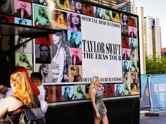 a young woman stands in front of sign that reads "Taylor Swift Eras Tour"