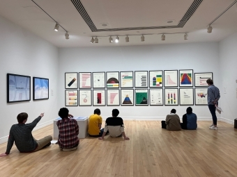 Students sitting at a gallery exhibition with art on the wall