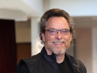 an older white man wearing a black shirt and a black vest with glasses