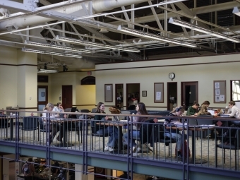 students work at tables in an open space with exposed ceiling