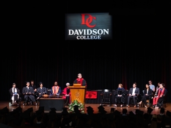 Convocation 2025 Doug Hicks speaking on stage with faculty and staff behind him