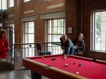 a group of people play pool in a brick building with big windows