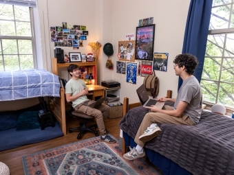 two young men sit in a dorm room talking and smiling with each other