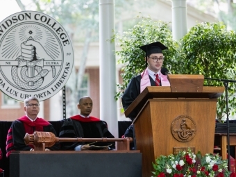 Commencement 2025 student speaker with Doug Hicks and Anthony Foxx in the background