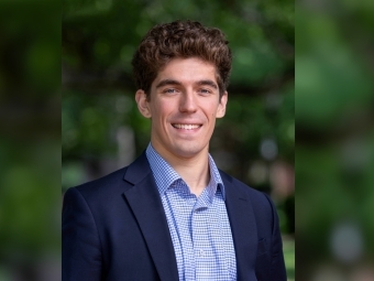 a young white man wearing a collared shirt and jacket with curly brown hair