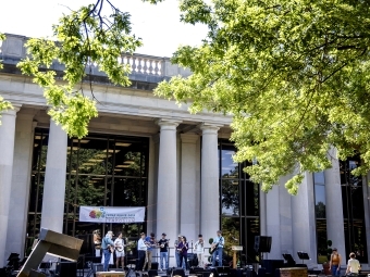 a group of students perform music in front of a columned academic building on a sunny day