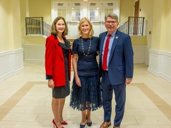 three people standing together in formal attire in a gallery space