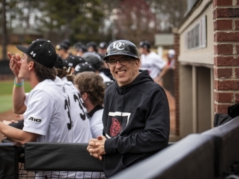 Man wearing Davidson gear smiles from Baseball dugout