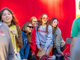 a group of young women and their moms pose in front of a red photo booth