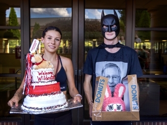 Two students holding elaborate cakes, one dressed as Batman