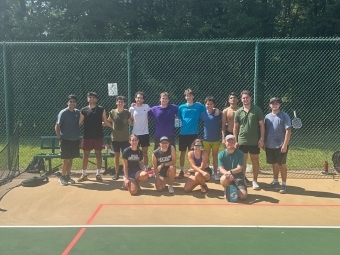 a group of students playing pickleball on an outdoor court on a sunny day